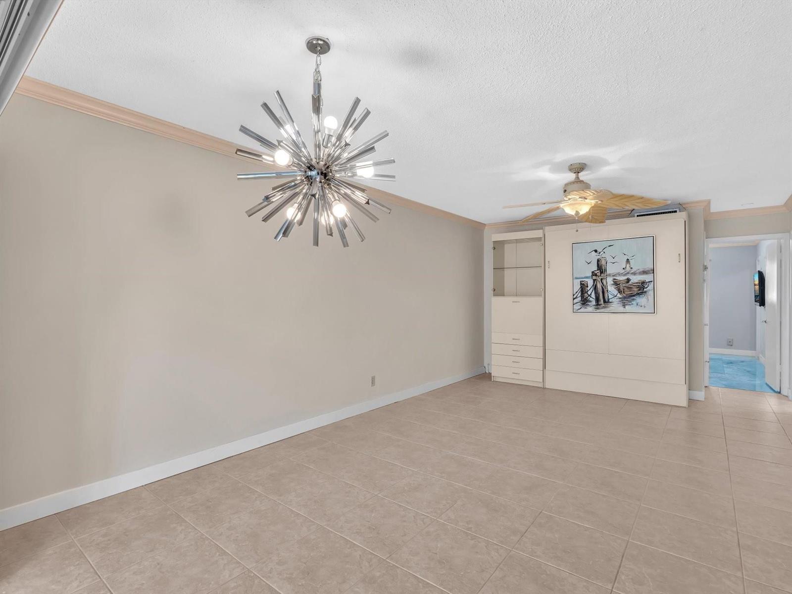 An empty room features beige tile flooring, a modern starburst chandelier, and a wall bed — 2000 Diana Drive # 207, Hallandale Beach FL 33009, HALLANDALE BEACH, FL