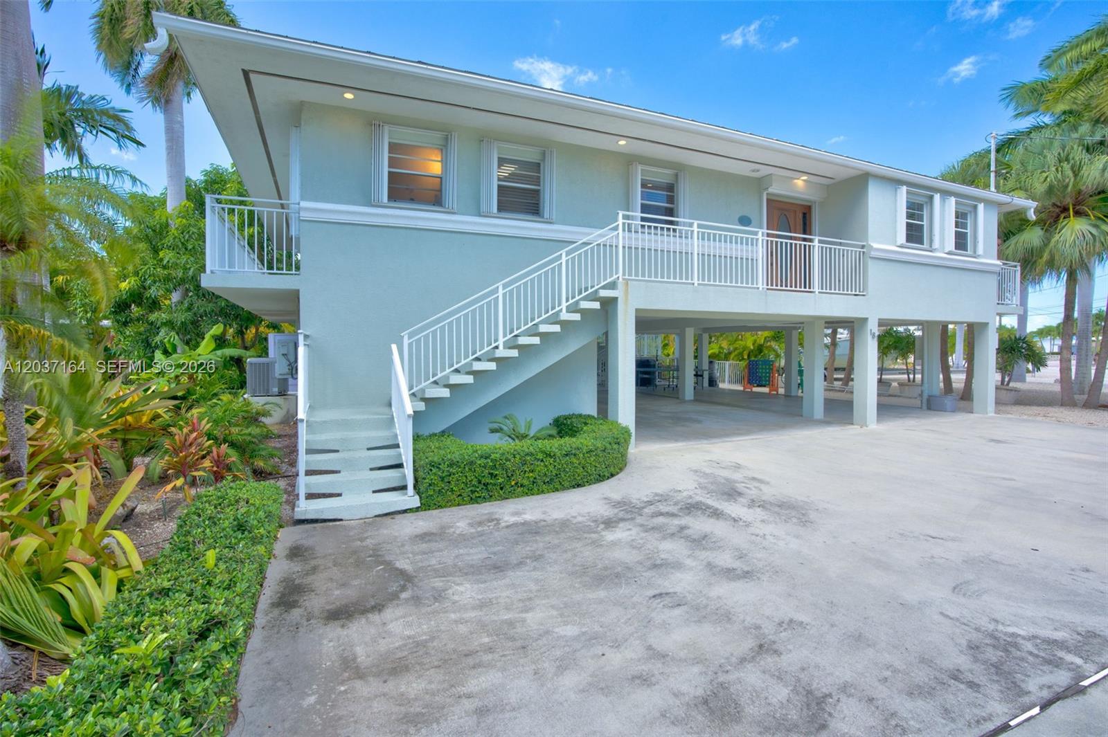 An elevated house with a white staircase leading to a porch and a concrete driveway — 181 12th St, Key Colony FL 33051, KEY COLONY, FL