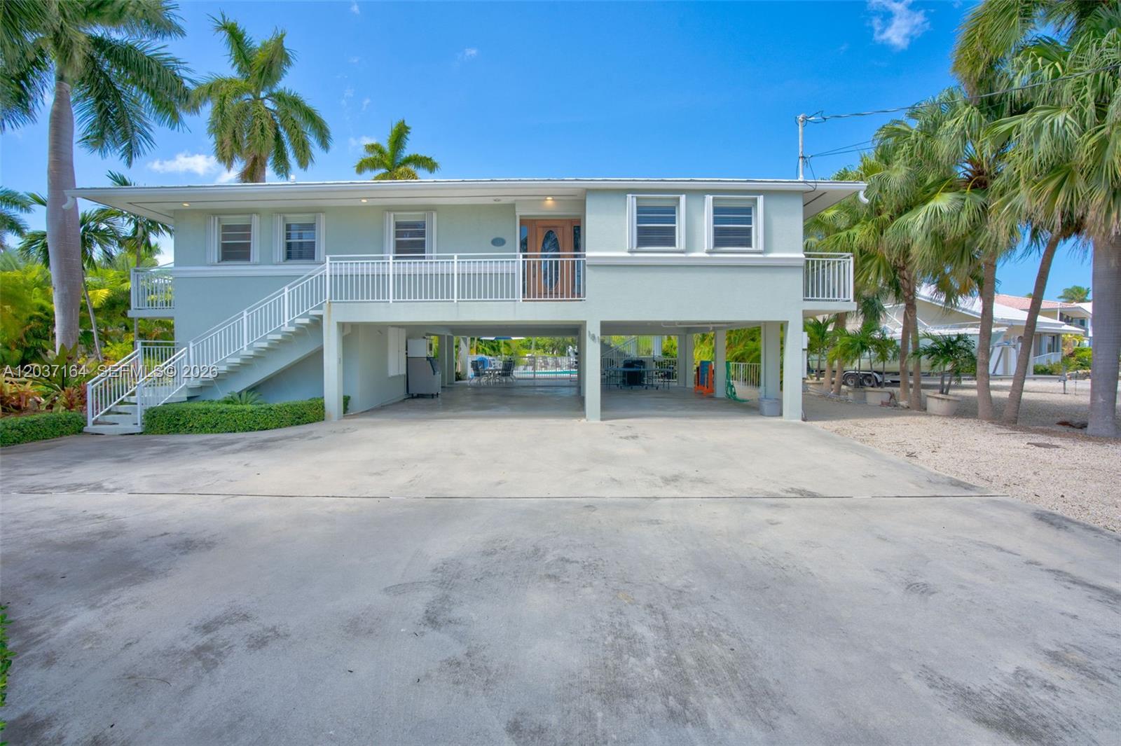 A light-colored elevated house features a concrete driveway, a staircase, and a covered ground level — 181 12th St, Key Colony FL 33051, KEY COLONY, FL