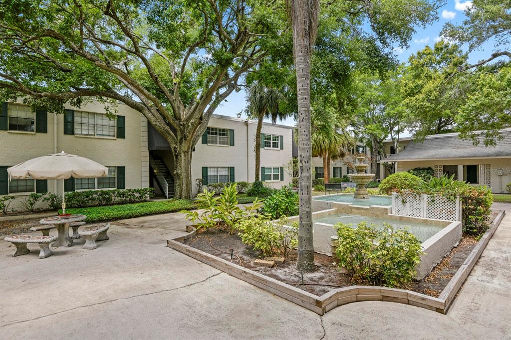 A courtyard features a tiered stone fountain, a patio table with an umbrella, and trees — 4335 AEGEAN DRIVE UNIT 254A, TAMPA, FL