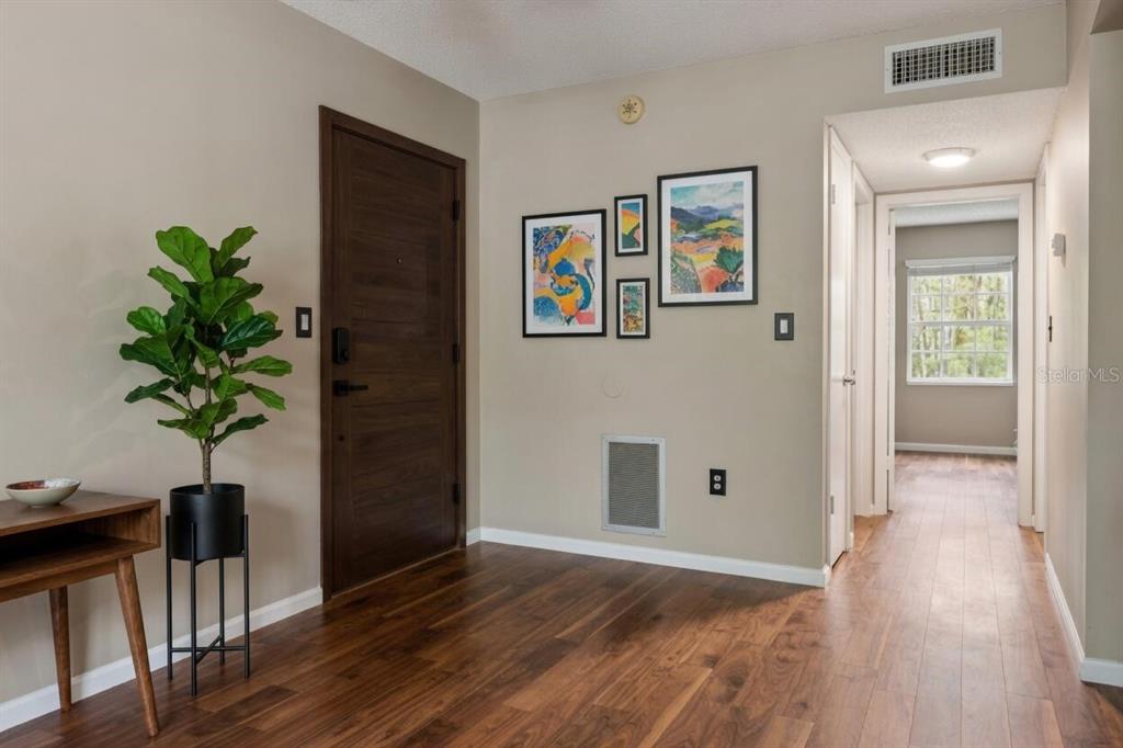 An entryway with wood flooring, a dark wood door, a potted plant, and wall art — 4335 AEGEAN DRIVE UNIT 254A, TAMPA, FL