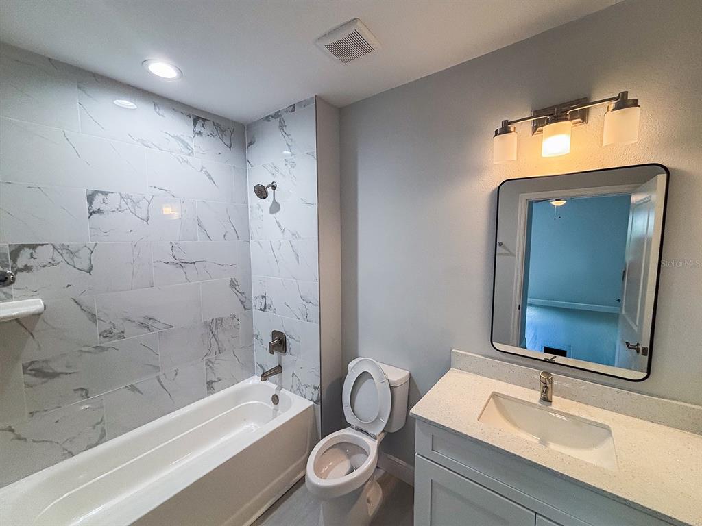 A bathroom features a marble-tiled shower-tub combo, a white vanity, and a wall-mounted mirror — 4508 LAFAYETTE AVENUE UNIT 4510, SEBRING, FL