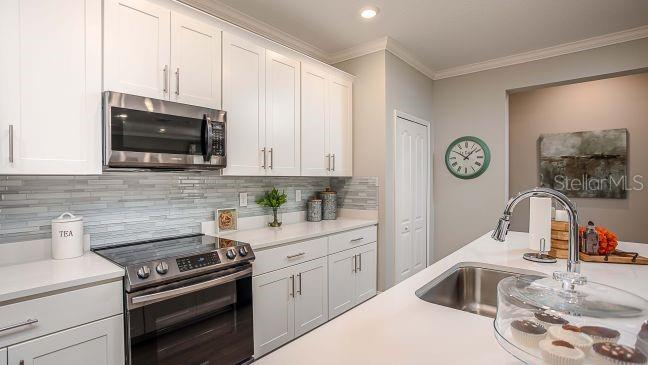 A kitchen with white cabinets, stainless steel appliances, a tiled backsplash, and a center island — 8623 OAKSTONE CIRCLE, LEESBURG, FL