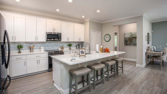 A modern kitchen features white cabinets, a large island with bar stools, and wood-look flooring — 8623 OAKSTONE CIRCLE, LEESBURG, FL
