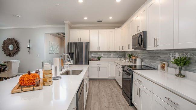 A modern kitchen features white cabinetry, quartz countertops, stainless steel appliances, and light wood flooring — 8623 OAKSTONE CIRCLE, LEESBURG, FL