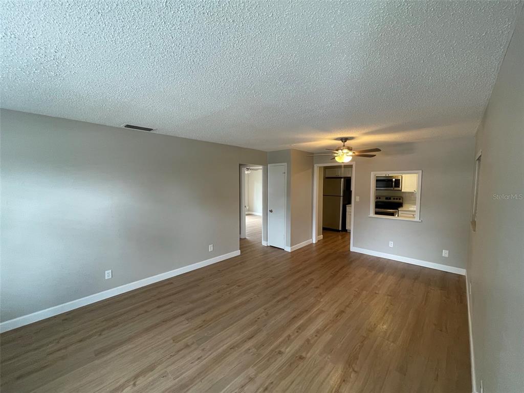 A living room with light gray walls, wood-look flooring, and a pass-through to the kitchen — 511 DUCHESS COURT UNIT 1, LAKELAND, FL