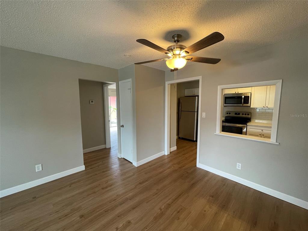 A room with wood-look flooring, a ceiling fan, and a pass-through window to the kitchen — 511 DUCHESS COURT UNIT 1, LAKELAND, FL