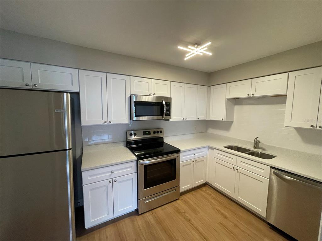 A kitchen features white cabinets, stainless steel appliances, light countertops, and wood-look flooring — 511 DUCHESS COURT UNIT 1, LAKELAND, FL