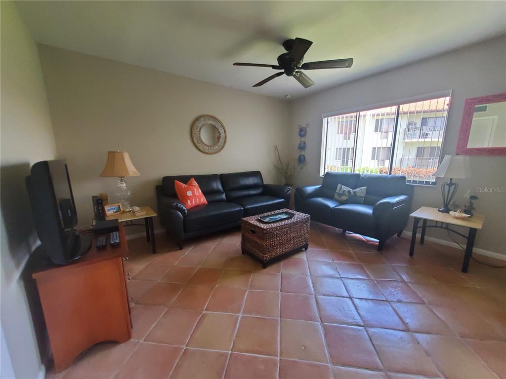 A living room features two black leather sofas, a wicker coffee table, and tile flooring — 1515 PINELLAS BAYWAY S UNIT 17, ST PETERSBURG, FL