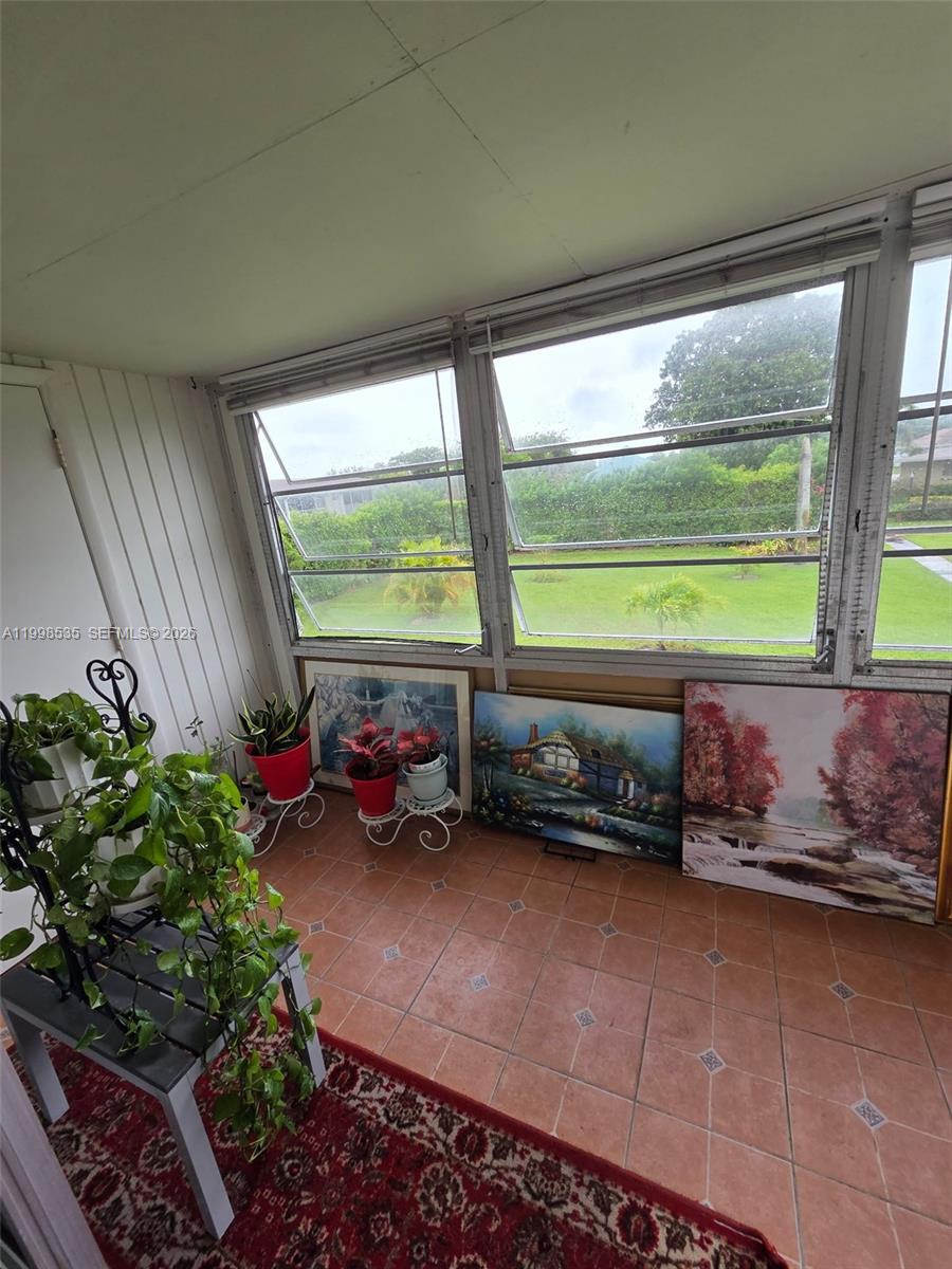 A sunroom features tiled floors, large windows overlooking a lawn, and several potted plants — 410 NE 17th Ave # 203, Boynton Beach FL 33435, BOYNTON BEACH, FL