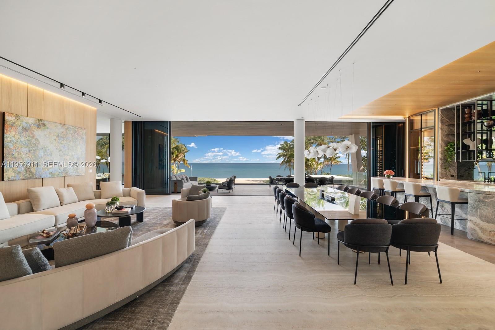 A modern open-concept living and dining area features floor-to-ceiling glass doors overlooking the ocean — 255 Ocean Blvd, Golden Beach FL 33160, GOLDEN BEACH, FL