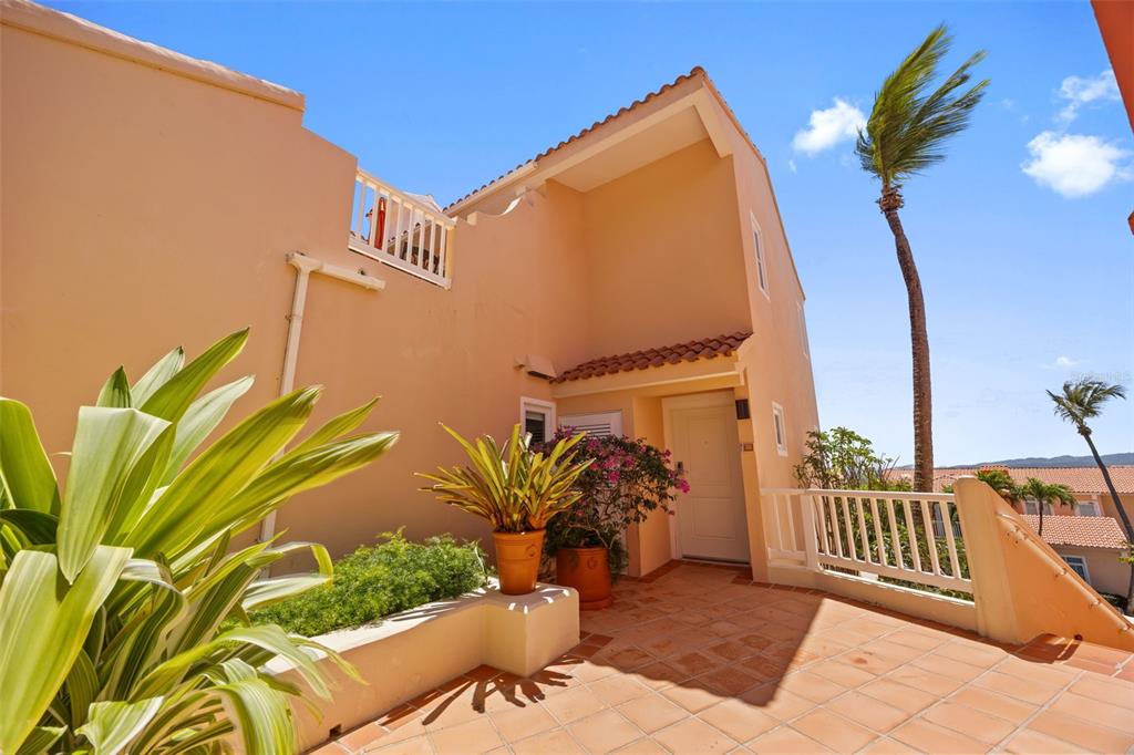 An exterior view of a peach-colored building entrance with a tiled patio and palm trees — 1000 AVENUE EL CONQUISTADOR UNIT 5151, FAJARDO, PR