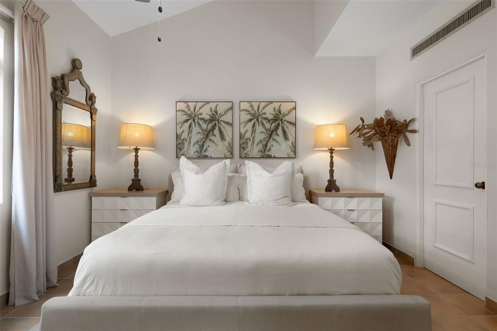 A bedroom features a bed with white bedding, two nightstands, lamps, and palm tree artwork — 1000 AVENUE EL CONQUISTADOR UNIT 5151, FAJARDO, PR