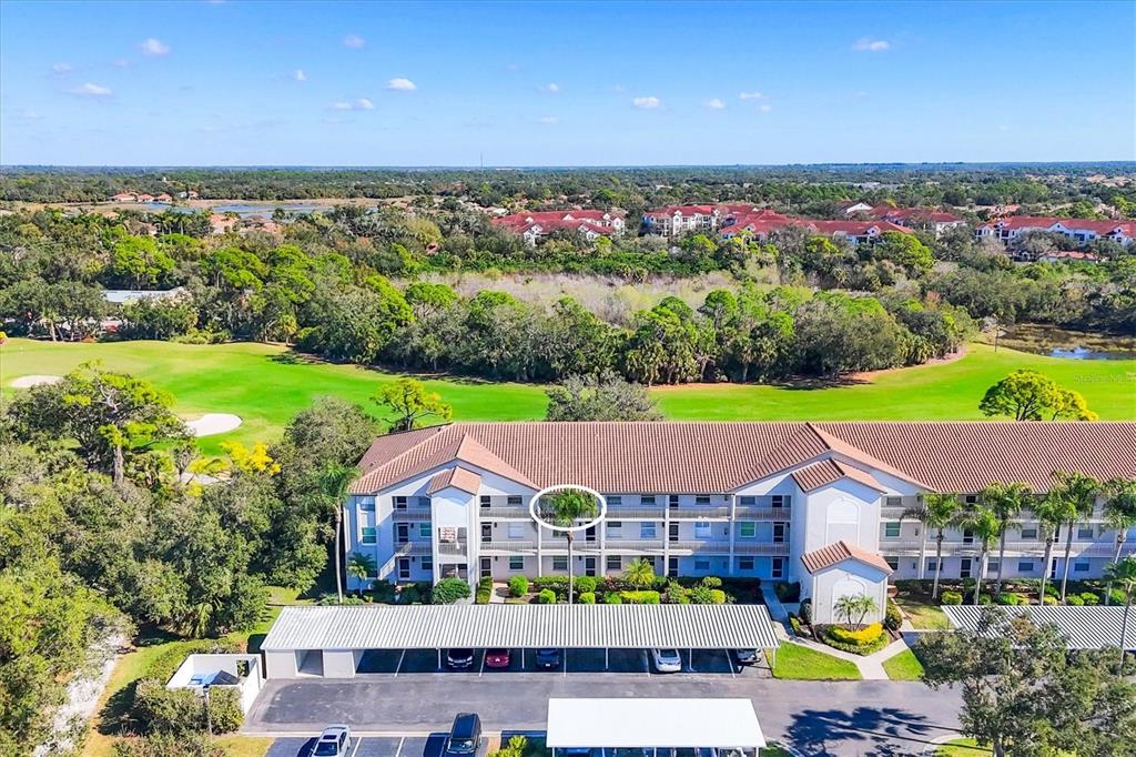 An aerial view shows a multi-story apartment building with a parking lot and golf course — 8735 OLDE HICKORY AVENUE UNIT 8303, SARASOTA, FL