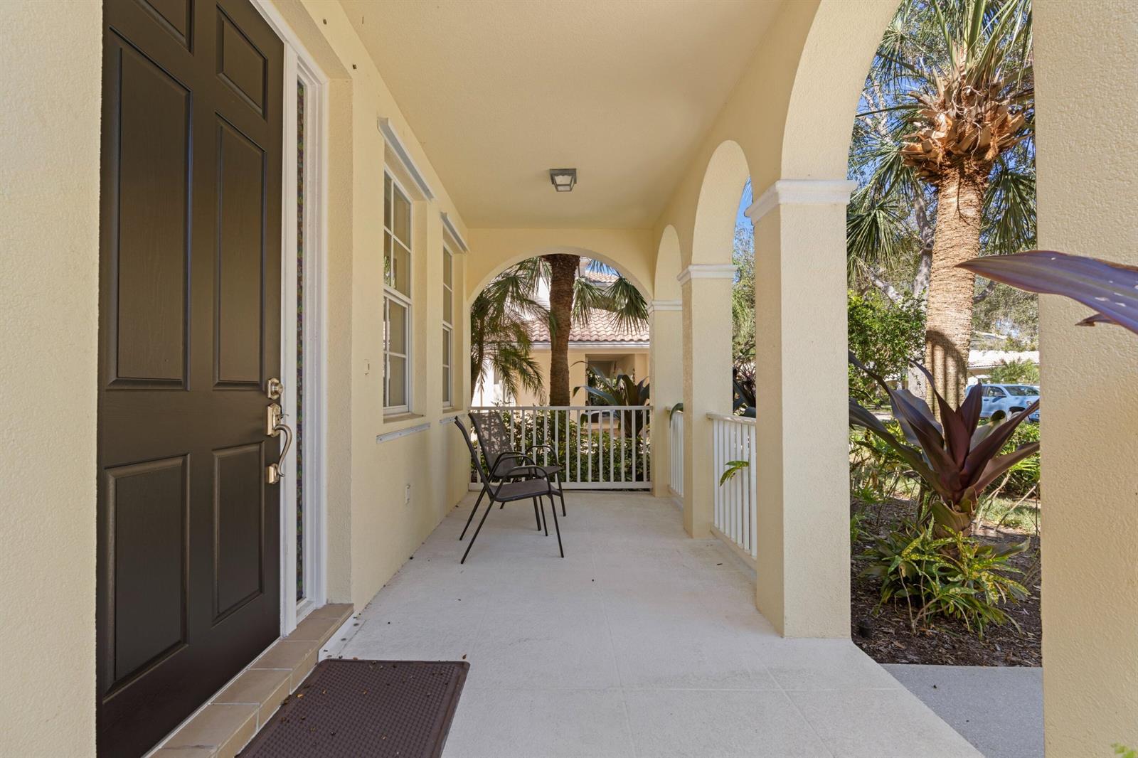 A covered porch features arched columns, a dark front door, and two chairs — 8418 Arima Lane, Wellington FL 33414, WELLINGTON, FL