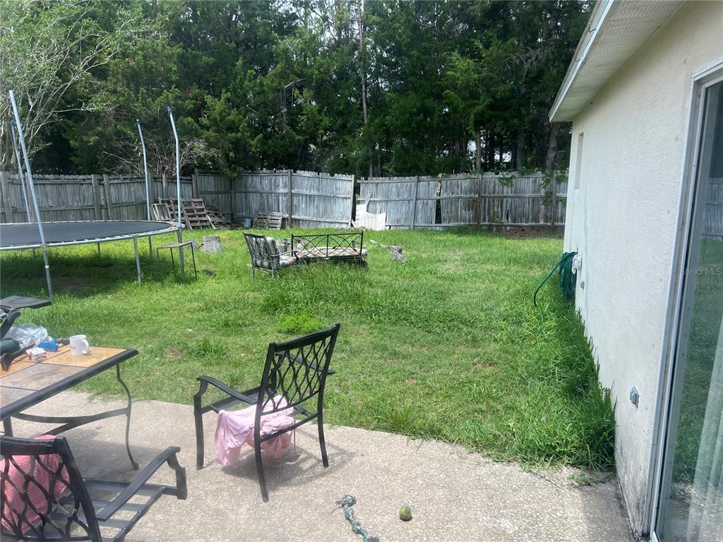 A backyard features a concrete patio, a trampoline, and a wooden fence — 69 RAEMOOR DRIVE, PALM COAST, FL