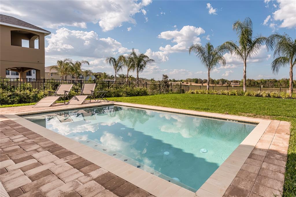 A rectangular swimming pool sits on a stone patio next to a grassy backyard — 7705 BANYON WAY, KISSIMMEE, FL