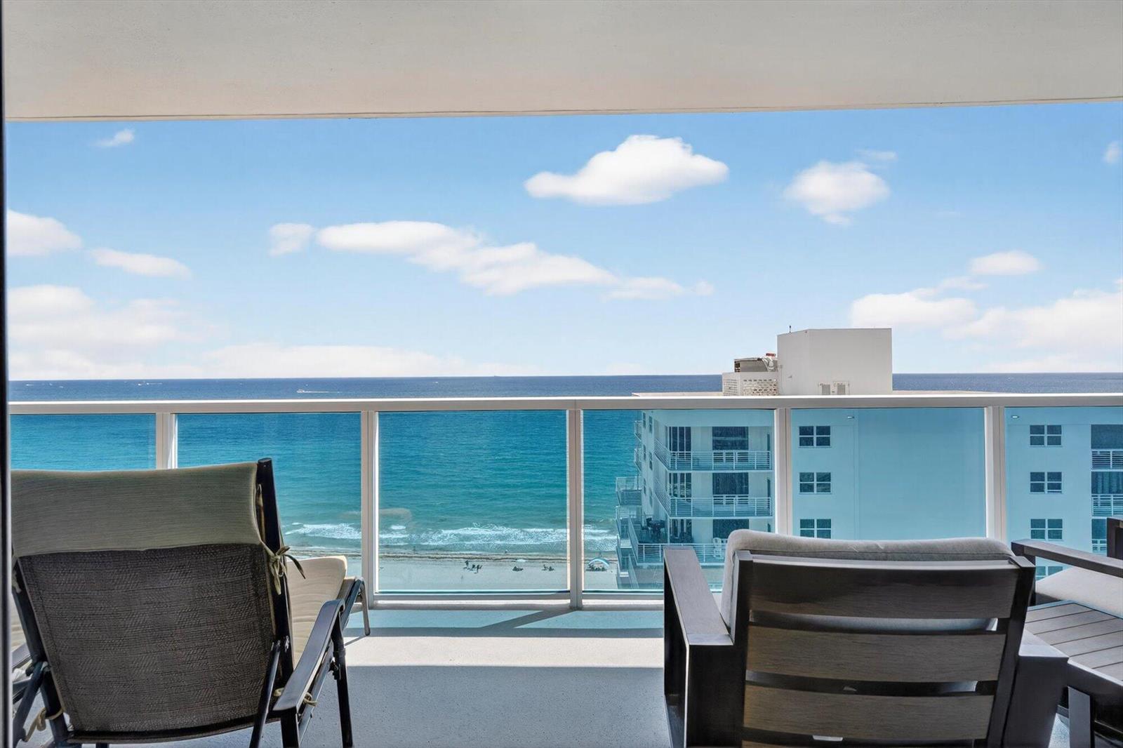 A balcony with two chairs overlooks the ocean and a neighboring building under a blue sky — 801 Briny Avenue # 1501, Pompano Beach FL 33062, POMPANO BEACH, FL