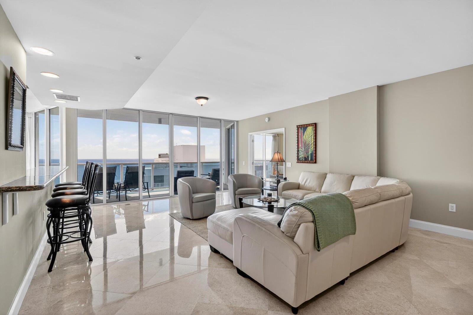 A living room features a beige sectional sofa, two armchairs, a breakfast bar, and balcony views — 801 Briny Avenue # 1501, Pompano Beach FL 33062, POMPANO BEACH, FL