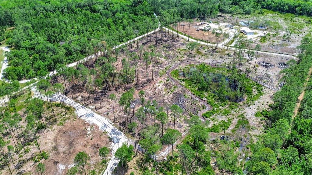 An aerial view shows a partially cleared wooded lot with dirt roads and nearby buildings — MARSHVIEW DRIVE, DELAND, FL