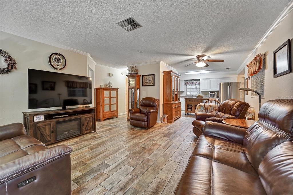A living room with wood-look tile flooring, leather furniture, and an open kitchen in back — 6642 DEVONSHIRE LANE, NEW PORT RICHEY, FL