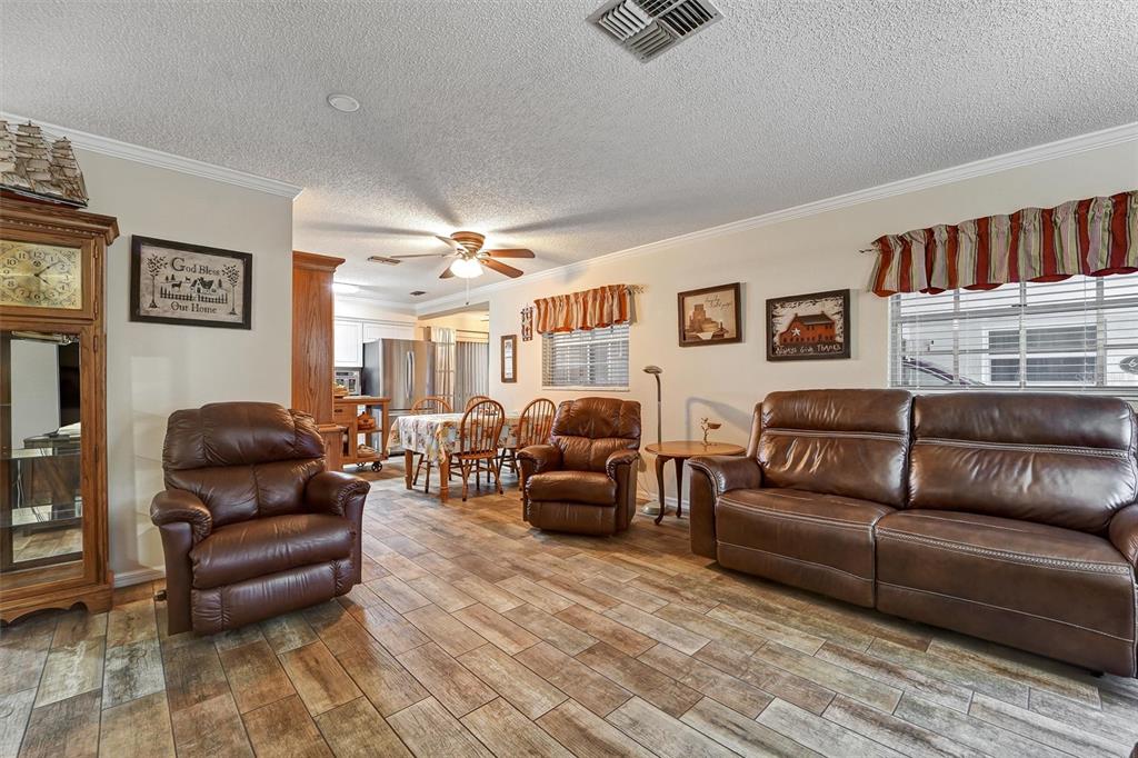 A living room features brown leather furniture, wood-look tile flooring, and an adjacent dining area — 6642 DEVONSHIRE LANE, NEW PORT RICHEY, FL