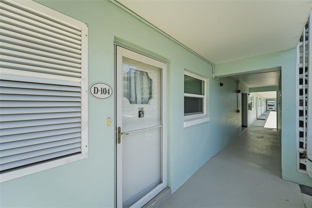 A light blue exterior hallway features a white door labeled D-104 with a storm door — 325 N CAUSEWAY UNIT D104, NEW SMYRNA BEACH, FL