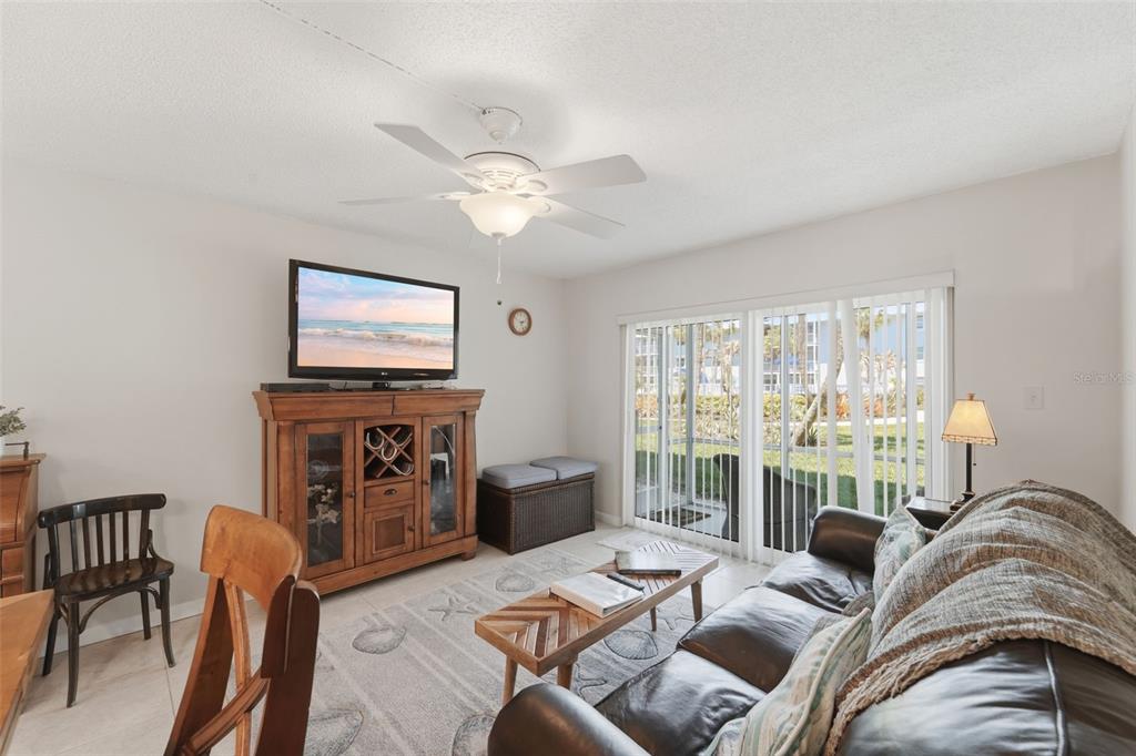 A living room features a ceiling fan, a television on a wooden cabinet, and sliding doors — 325 N CAUSEWAY UNIT D104, NEW SMYRNA BEACH, FL