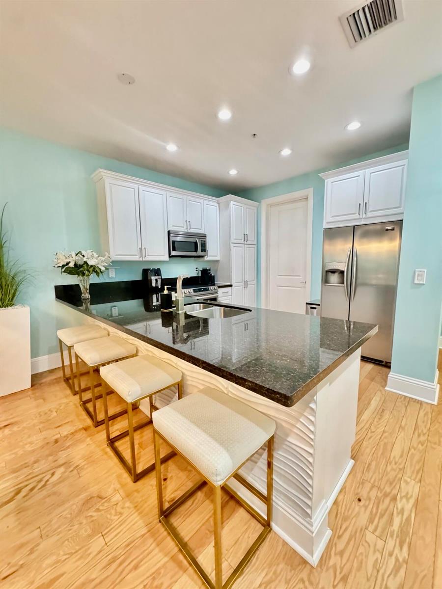 A kitchen with white cabinets, black countertops, stainless steel appliances, and light wood flooring — 3120 E Latitude Circle E # 101s, Delray Beach FL 33483, DELRAY BEACH, FL
