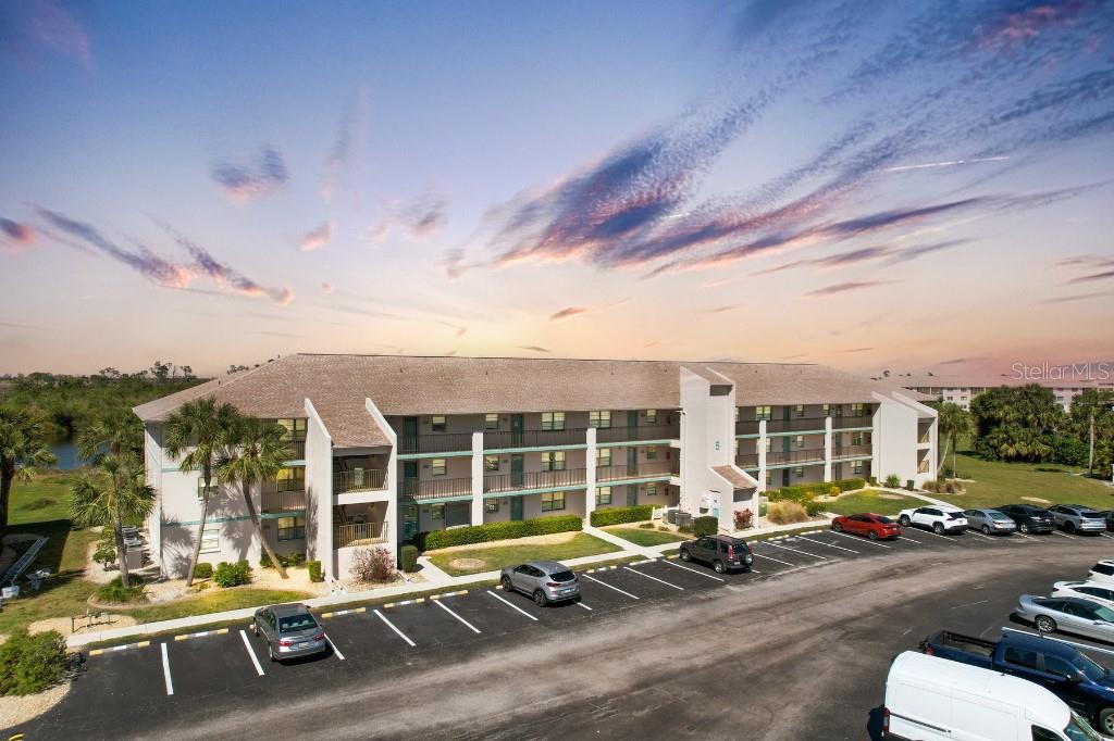 An aerial view of a multi-story apartment building with a parking lot at sunset — 175 KINGS HIGHWAY UNIT 514, PUNTA GORDA, FL