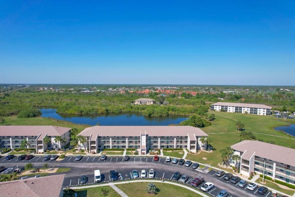 An aerial view shows multi-story apartment buildings, a parking lot, and a pond — 175 KINGS HIGHWAY UNIT 514, PUNTA GORDA, FL