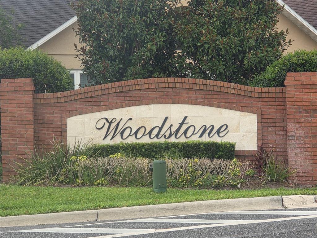 A brick entrance sign for a community named Woodstone sits in front of green landscaping — 7935 OAKSTONE COURT, ORLANDO, FL