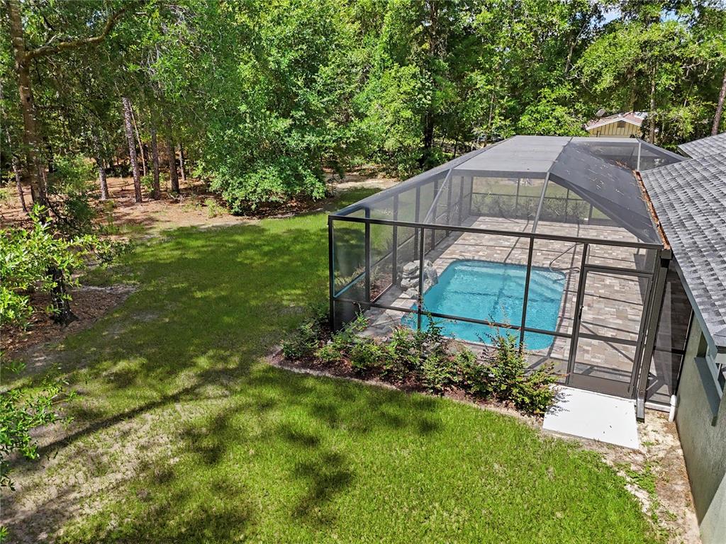 An elevated view of a screened-in pool and patio area adjacent to a grassy backyard — 20638 SW 88 PLACE ROAD, DUNNELLON, FL