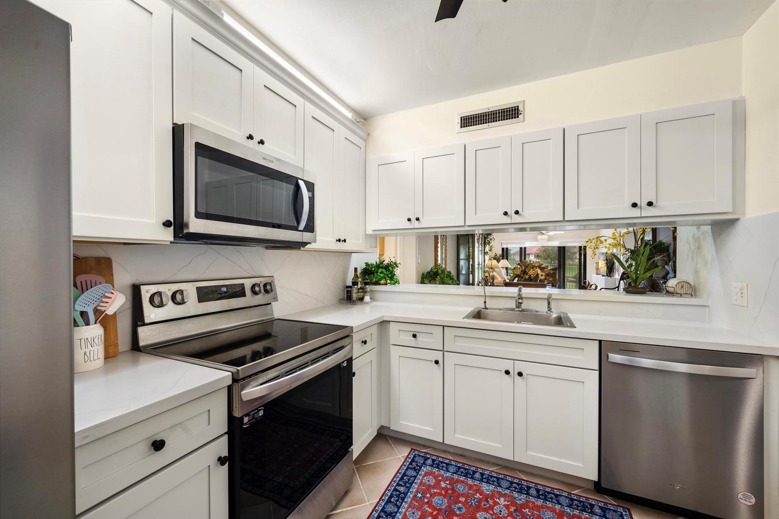A kitchen with white cabinets, stainless steel appliances, and a pass-through window to the living area — 601 Seafarer Circle # 104, Jupiter FL 33477, JUPITER, FL