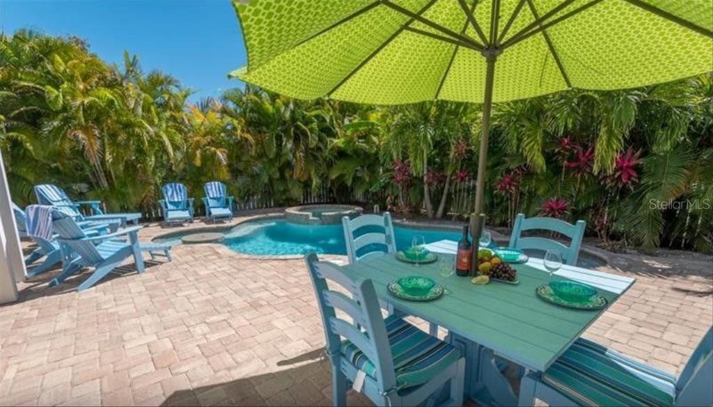 A patio with a dining set and lounge chairs overlooks a swimming pool and spa — 117 WILLOW AVENUE, ANNA MARIA, FL