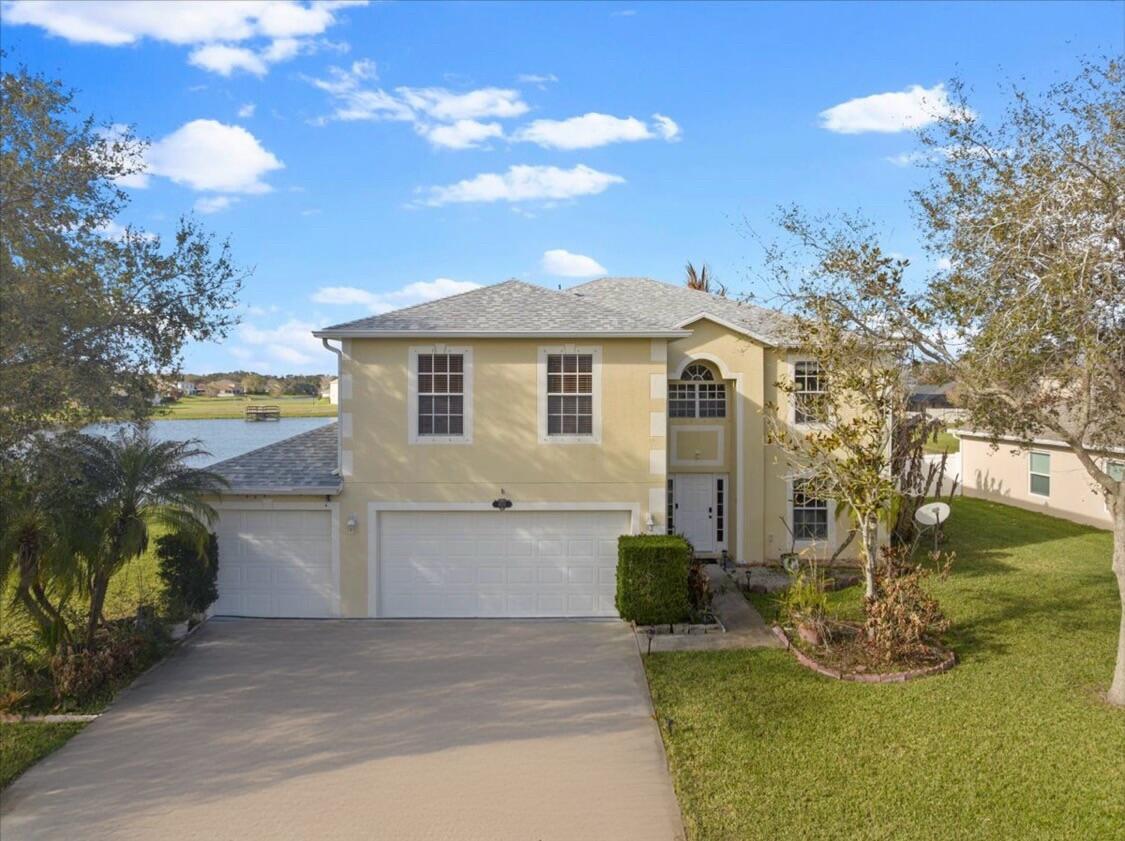 An aerial view of a two-story yellow house with a gray roof beside a lake — 6052 Ridge Lake Circle, Vero Beach FL 32967, VERO BEACH, FL