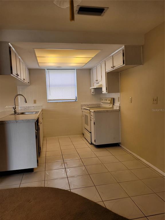 A kitchen features white cabinets, tiled flooring, a window, and a white stove — 5814 LIDDELL DRIVE, NEW PORT RICHEY, FL