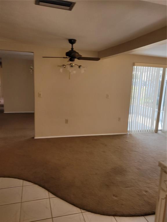 A living room features beige carpet, a ceiling fan, and a sliding glass door — 5814 LIDDELL DRIVE, NEW PORT RICHEY, FL