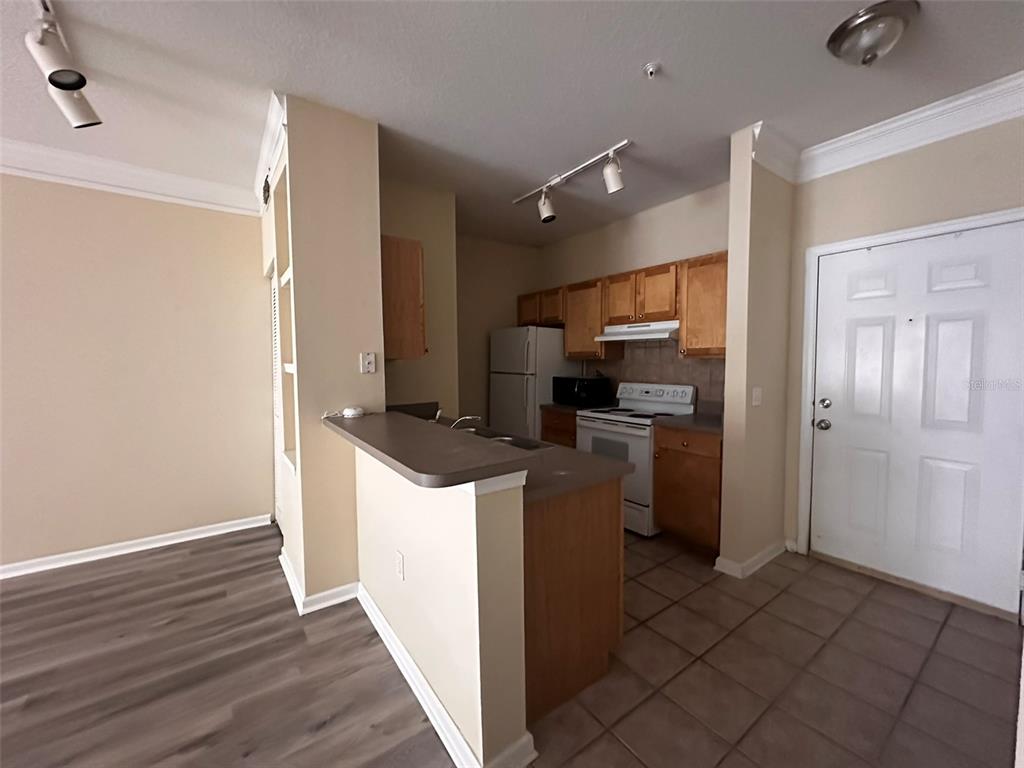 A kitchen with wood cabinets, white appliances, and a breakfast bar overlooks a living area — 4207 S DALE MABRY HIGHWAY UNIT 2103, TAMPA, FL
