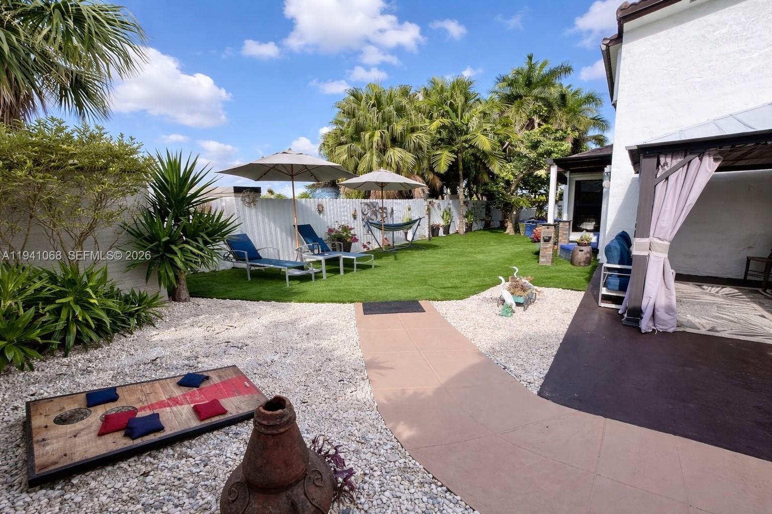 A backyard features a gravel area with a cornhole game, a walkway, and a lawn — 8618 SW 161st Pl, Miami FL 33193, MIAMI, FL