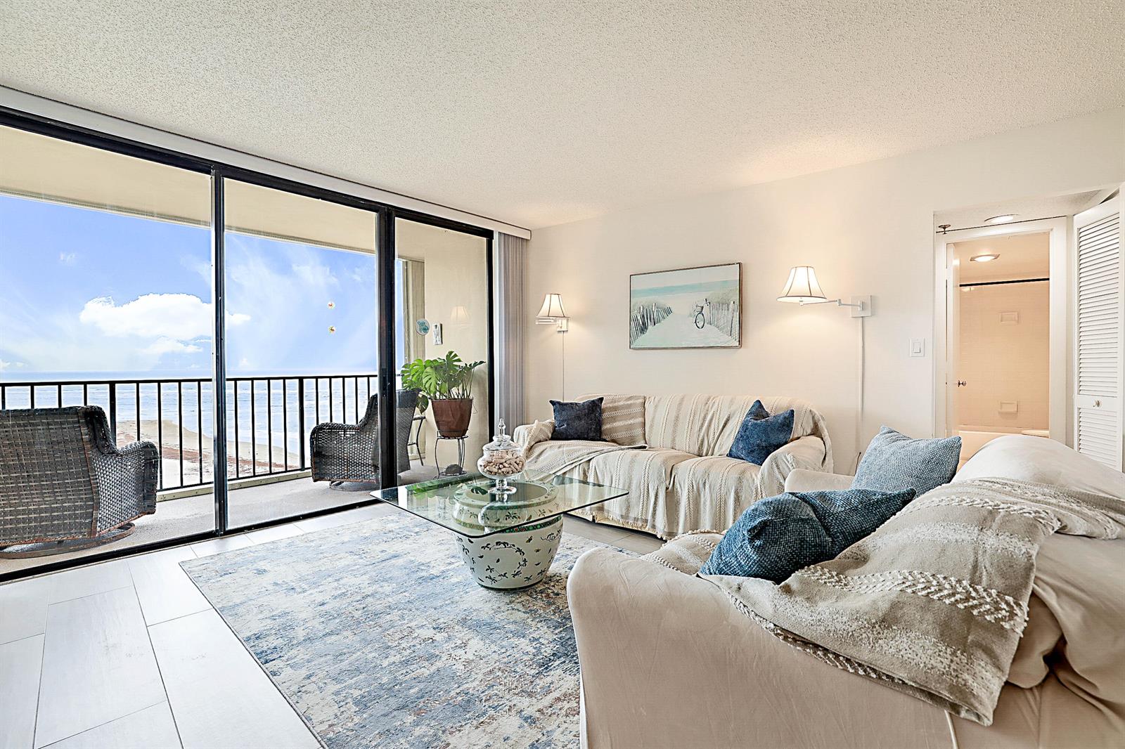 A living room with a glass coffee table, two sofas, and a balcony overlooking the ocean — 100 Ocean Trail Way # 1003, Jupiter FL 33477, JUPITER, FL
