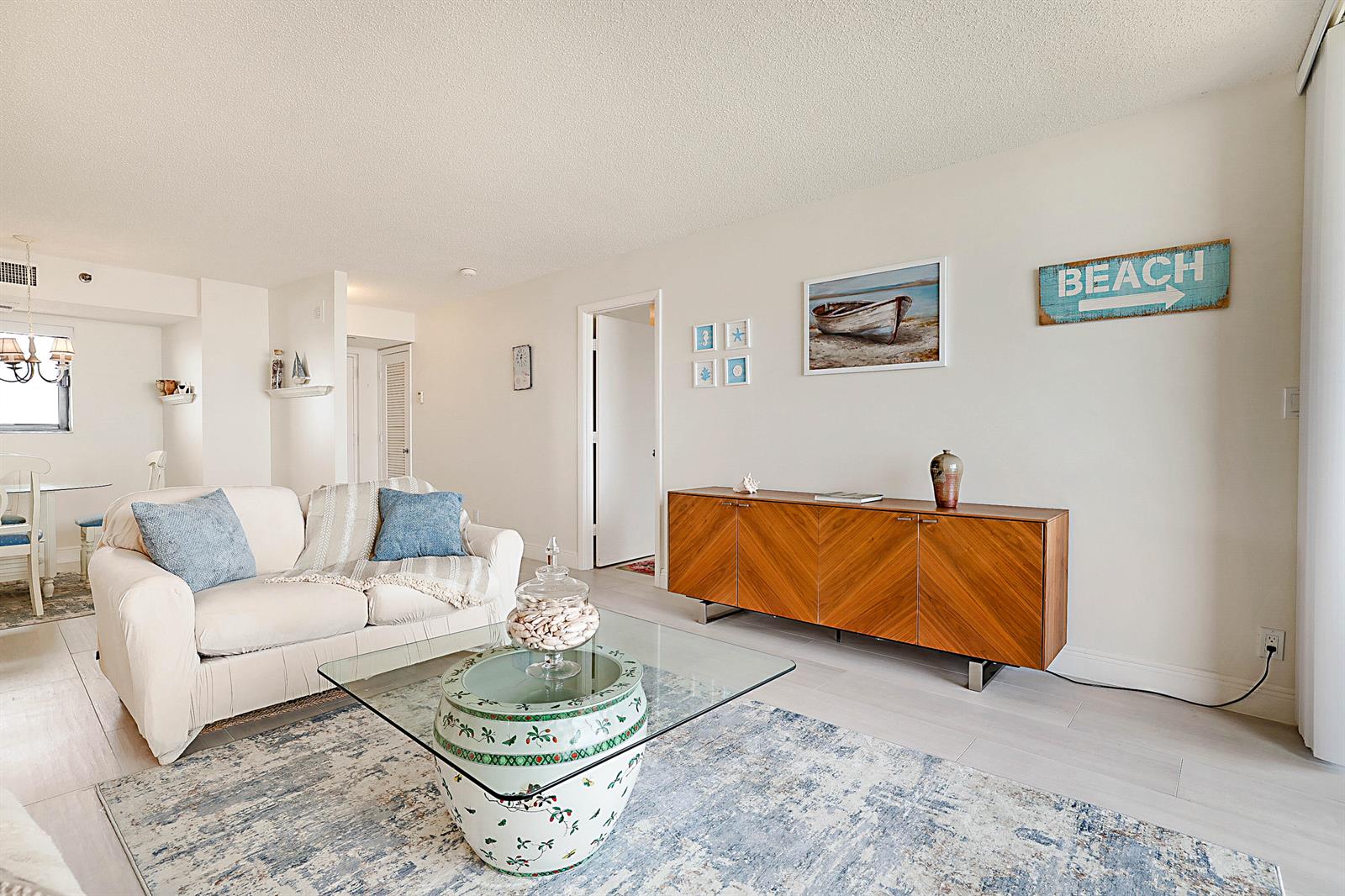 A living room features a white sofa, glass coffee table, and a wooden sideboard — 100 Ocean Trail Way # 1003, Jupiter FL 33477, JUPITER, FL