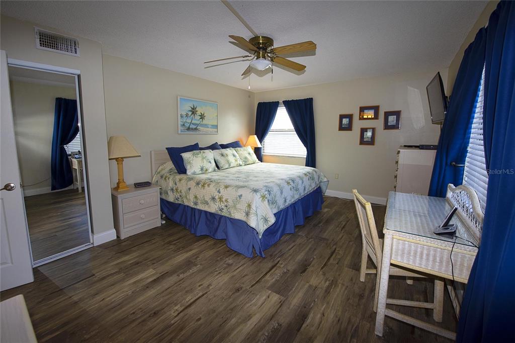 A bedroom features a king bed, wood-look flooring, a desk, and a mirrored closet door — 1571 S ATLANTIC AVENUE UNIT 201, NEW SMYRNA BEACH, FL