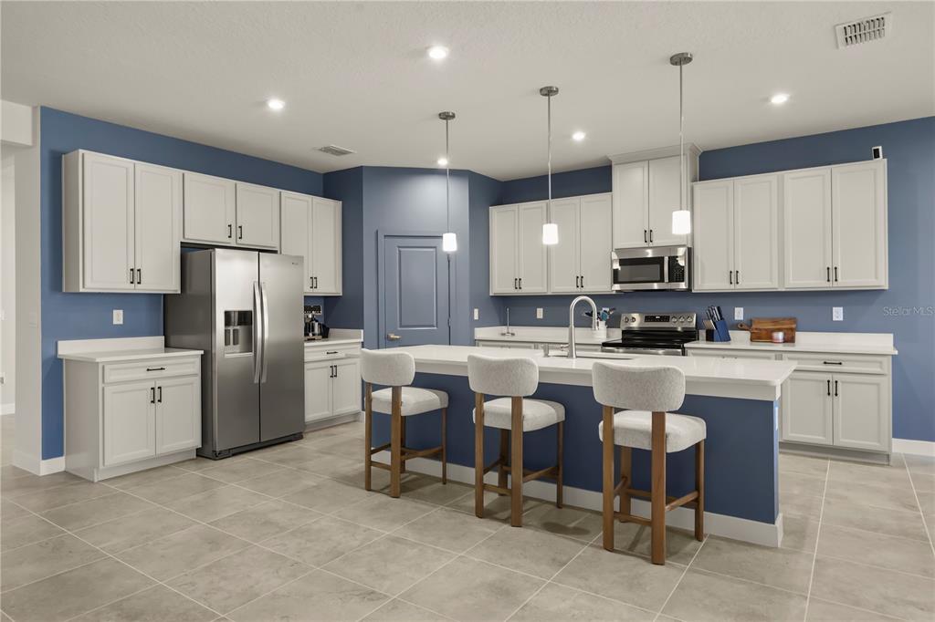 A kitchen features white cabinets, blue walls, a large island with seating, and stainless appliances — 1714 UPLAND LANE, WINTER HAVEN, FL