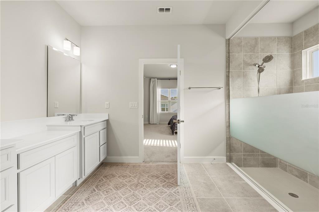 A bathroom features a white vanity, a walk-in shower with tile walls, and a doorway — 1714 UPLAND LANE, WINTER HAVEN, FL