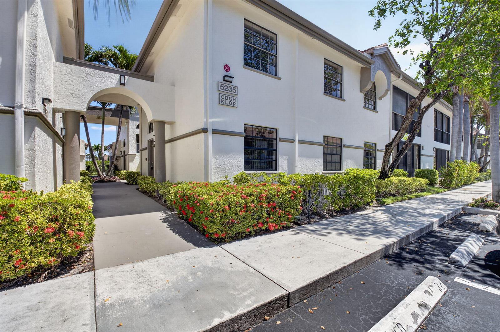 A two-story white stucco apartment building features an arched entryway and manicured landscaping — 5235 Europa Drive Apt L, Boynton Beach FL 33437, BOYNTON BEACH, FL