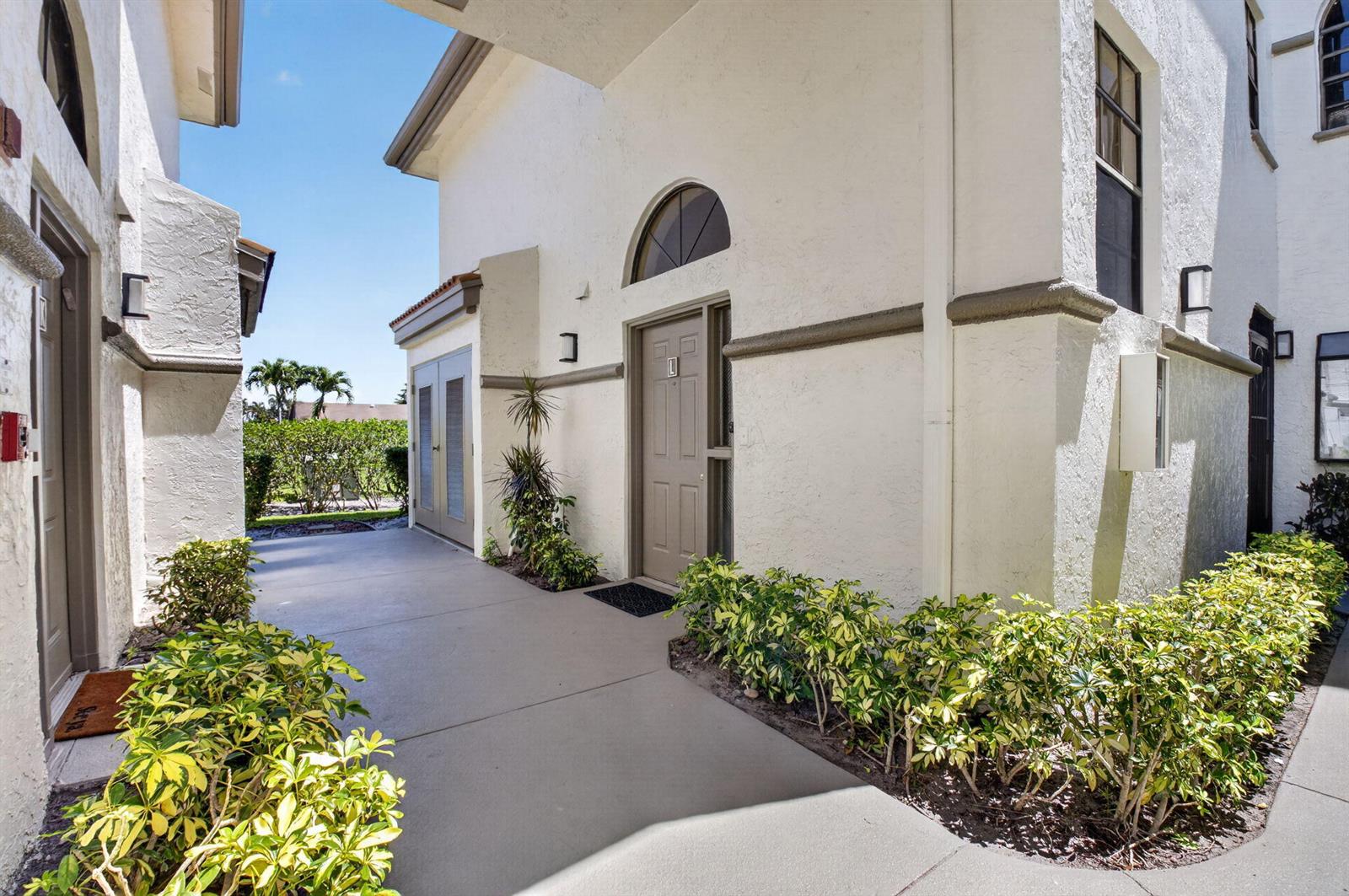 A concrete walkway leads to the entrance of a white stucco building with arched windows — 5235 Europa Drive Apt L, Boynton Beach FL 33437, BOYNTON BEACH, FL
