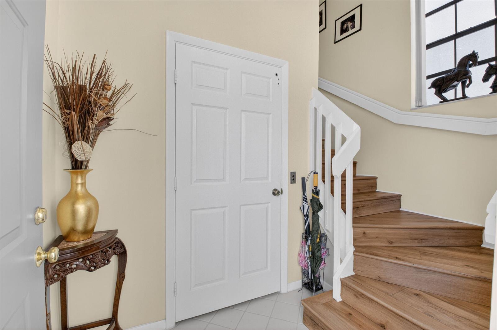 An entryway features a wooden staircase, a white door, and a gold vase on a table — 5235 Europa Drive Apt L, Boynton Beach FL 33437, BOYNTON BEACH, FL