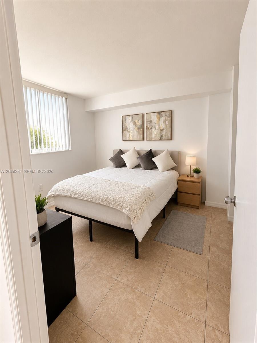 A bedroom features a bed with a white comforter, two nightstands, and tile flooring — 102 SW 6th Ave # 205, Miami FL 33130, MIAMI, FL