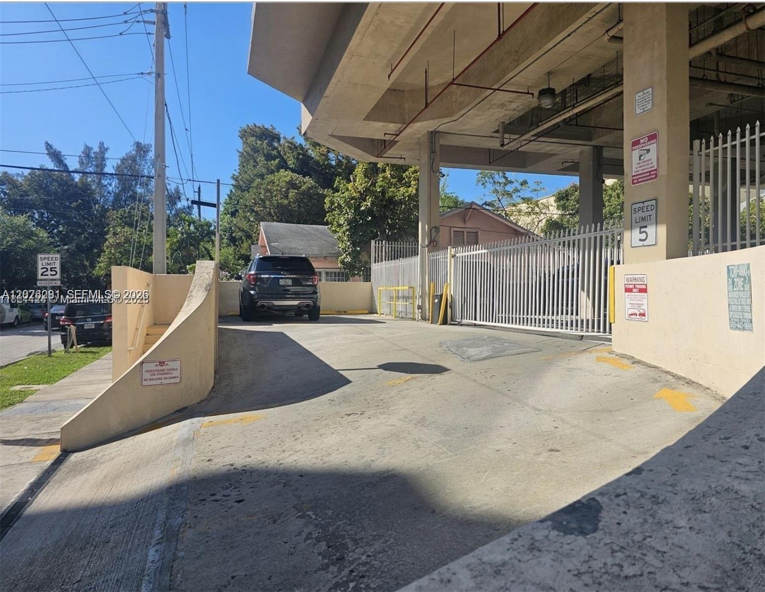 A concrete ramp leads to a gated parking garage entrance next to a residential street — 102 SW 6th Ave # 205, Miami FL 33130, MIAMI, FL